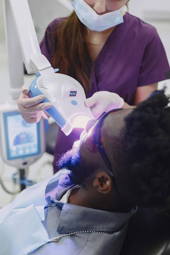 Dentist operating a light-curing machine for in-office teeth whitening on a male patient