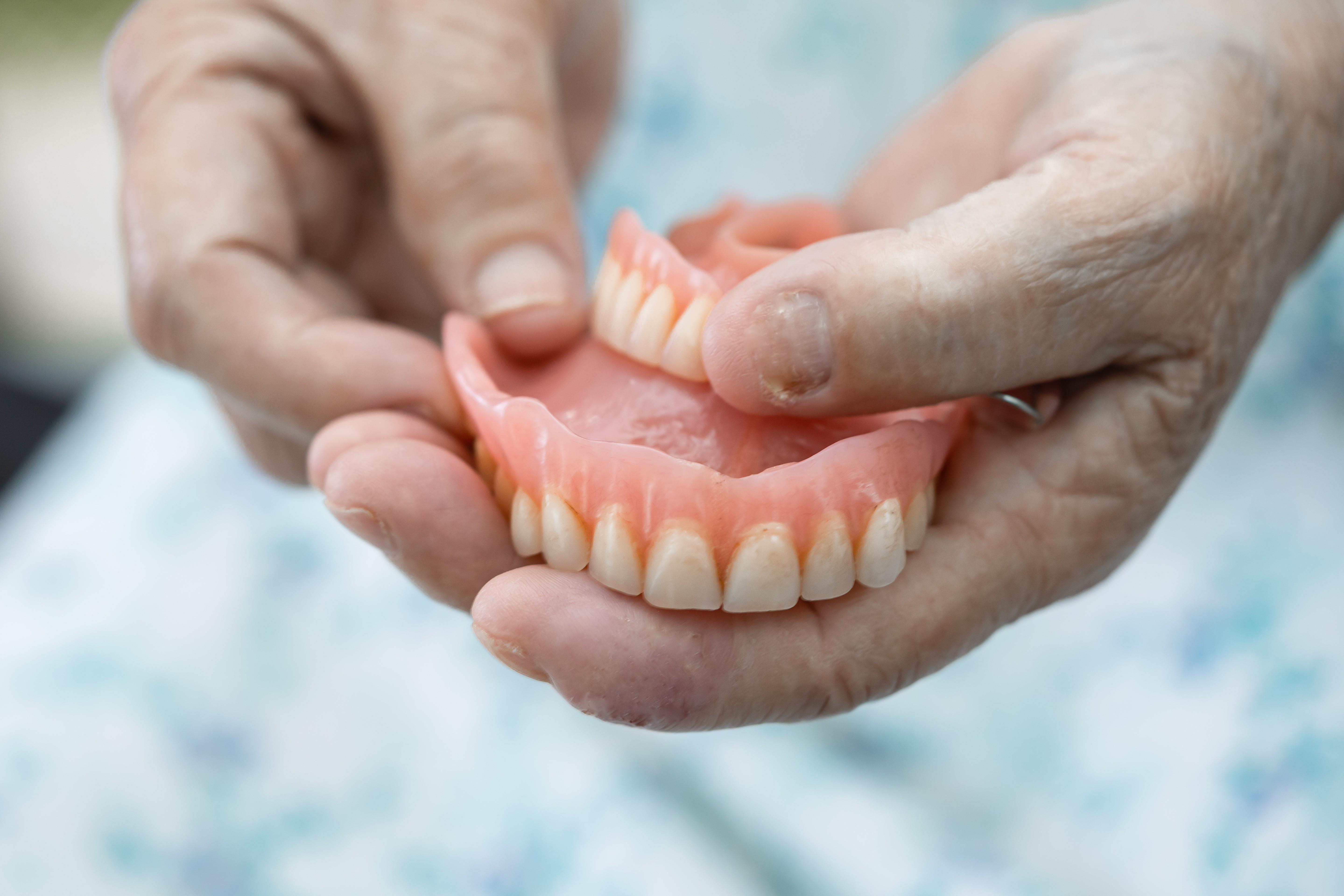 A person's hands holding a full set of dentures