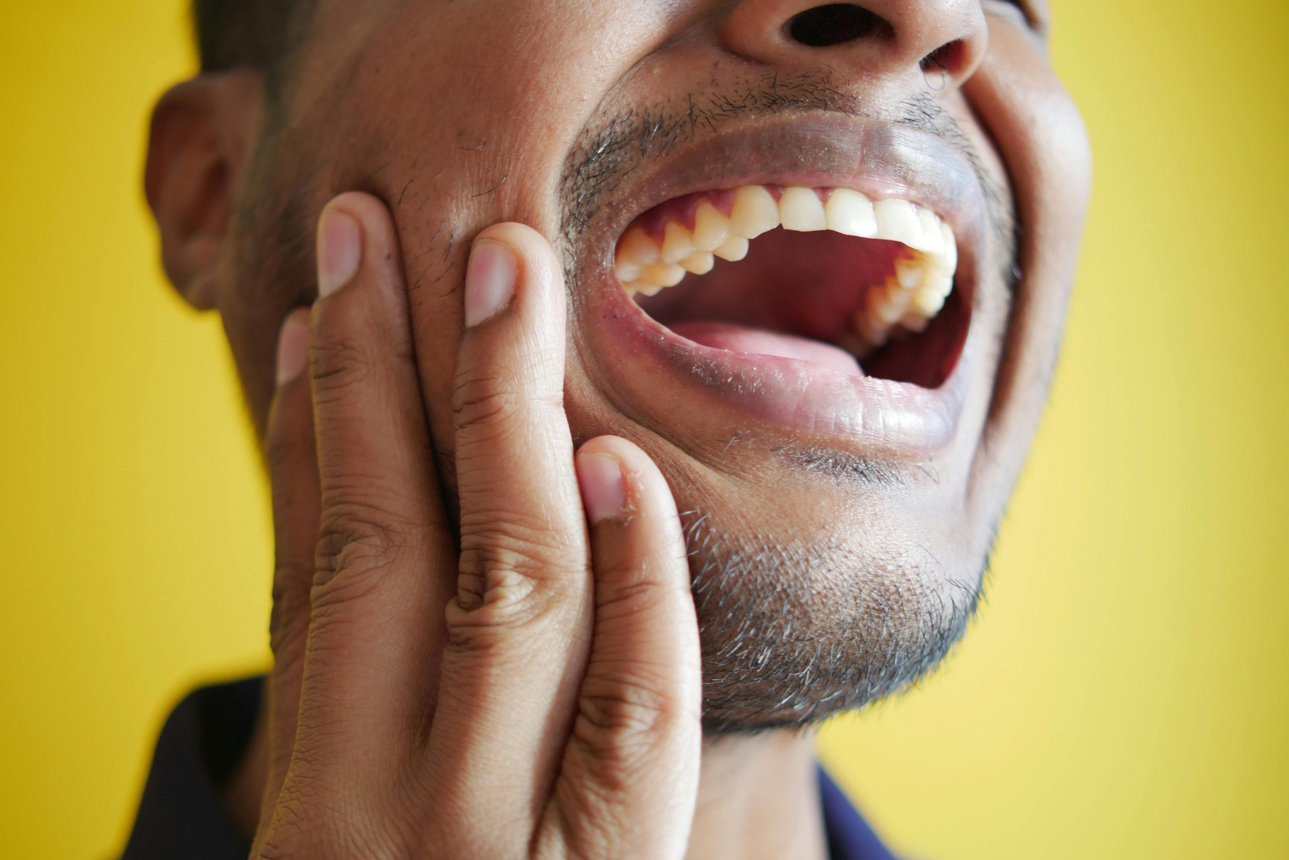 A man grimacing and holding his hand to his jaw, indicating severe toothache