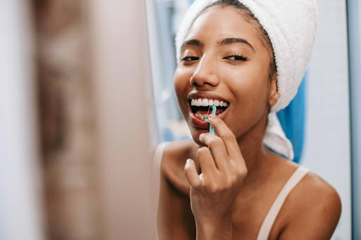 A smiling woman using a blue floss pick to clean her teeth