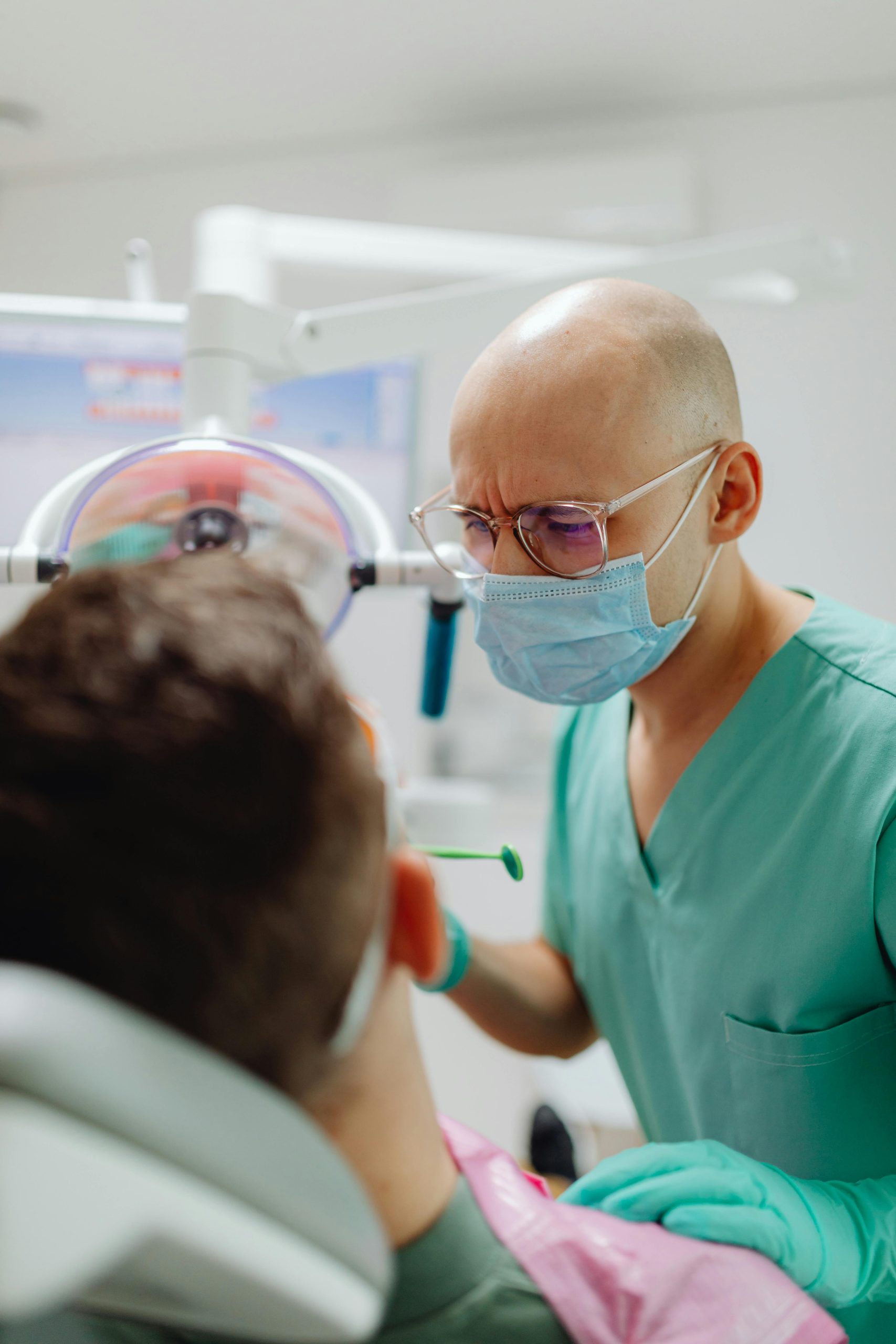 dentist-performing-oral-exam A dentist in a surgical mask performs a close examination of a patient in a dental chair