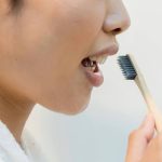 A woman brushing her teeth with a bamboo toothbrush